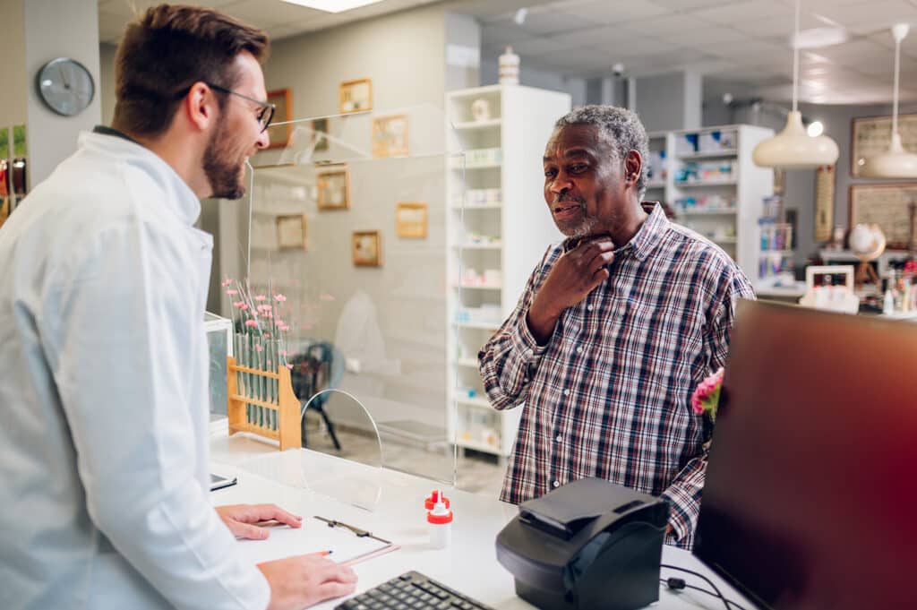 Pharmacist talking to an older male patient in a pharmacy.